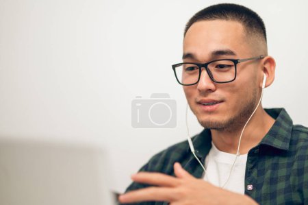 Photo for Portrait of a male in wireless earbuds looking at the laptop screen during the video call - Royalty Free Image