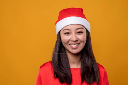 Téléchargez les photos : Joli père Noël. Mignon asiatique souriant jeune femme dans santa chapeau - en image libre de droit