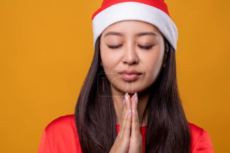 Téléchargez les photos : Prière de Noël. Jeune femme au chapeau de Père Noël priant les yeux fermés - en image libre de droit
