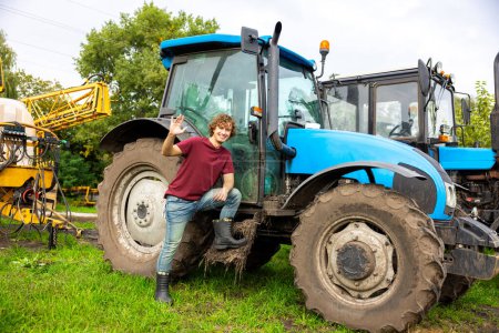 Photo for Full-size portrait of a smiling happy young man standing at the tractor and greeting somebody - Royalty Free Image