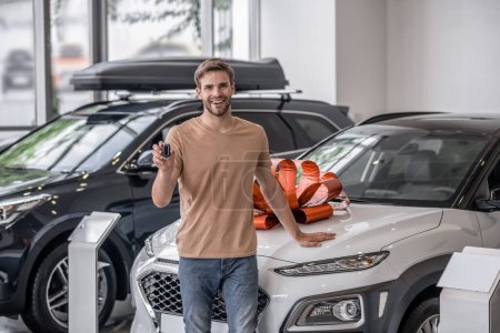 Photo for New car. Happy young car owner standing near his new car in a car salon - Royalty Free Image