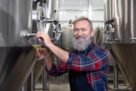 Photo for Fresh product. Brewery worker pouring fresh beer into the glass - Royalty Free Image