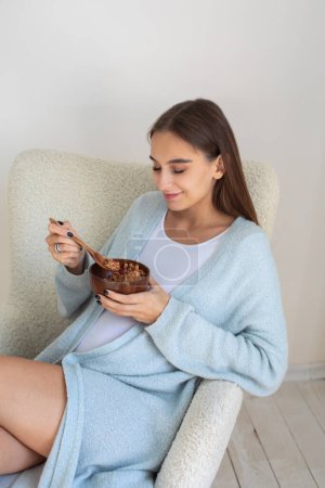 Photo for Healthy breakfast. Cute pregnant woman eating healthy food and looking contented - Royalty Free Image