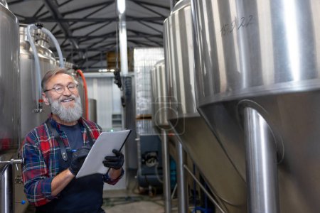 Foto de Control. Hombre de camisa a cuadros revisando los tanques con cerveza en la cervecería - Imagen libre de derechos