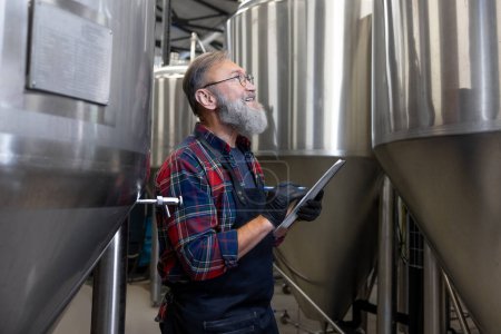 Photo for Control. Man in plaid shirt checnking the tanks with beer at the brewery - Royalty Free Image