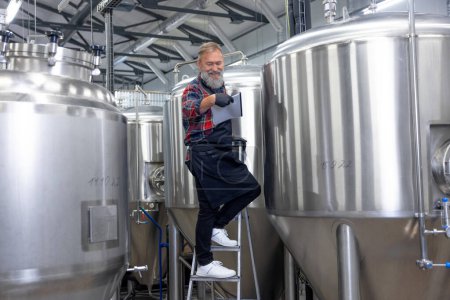 Téléchargez les photos : Good result. Factory worker checking the tanks with beer and looking satisfied with the result - en image libre de droit