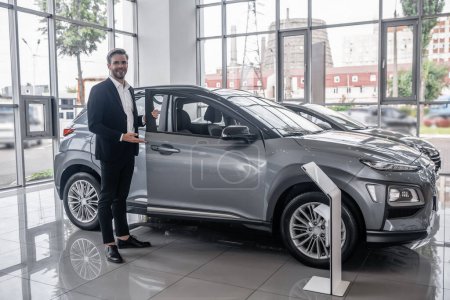 Téléchargez les photos : New model. Good-looking salesperson presenting a new vehicle in a car dealership - en image libre de droit