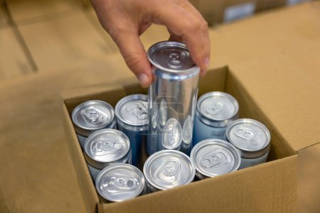 Photo for Close-up of a male hand putting a sealed aluminum can into the open cardboard box - Royalty Free Image