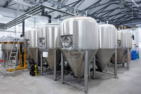 Téléchargez les photos : Pressure washer and a step ladder placed next to numerous stainless steel beer fermentation tanks - en image libre de droit