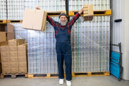 Téléchargez les photos : Full-size portrait of a joyful man in workwear holding pieces of cardboard in his hands - en image libre de droit