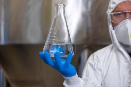 Photo for Cropped photo of a brewer in a nitrile glove holding a graduated flask with clear liquid - Royalty Free Image