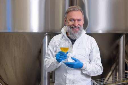 Foto de Waist-up portrait of a smiling contented brewer in nitrile gloves holding a glass of fresh beer - Imagen libre de derechos