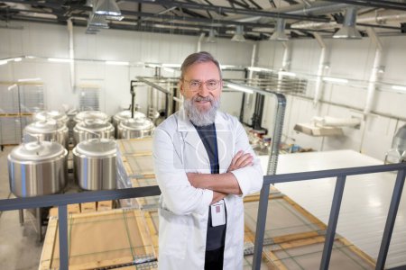 Téléchargez les photos : Mature technologist in a lab coat and eyeglasses standing with his arms crossed at a brewery - en image libre de droit