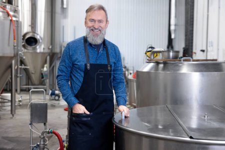 Photo for At the beer brewery. Factory worker standing near the tank with beer - Royalty Free Image