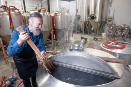 Téléchargez les photos : Stirring beer. Brewery worker stirring fresh beer in a tank - en image libre de droit