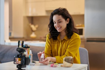 Foto de Beauty tricks. Smiling young woman demonstrating new foundation cream on online tutorial - Imagen libre de derechos