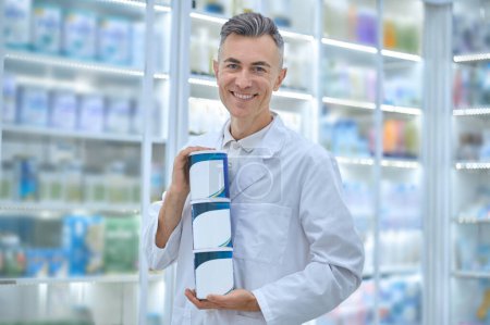 Foto de Infant milk. Smiling male pharmacist with cans of infant milk in hands - Imagen libre de derechos