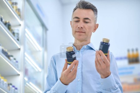Photo for Healthcare. Short-haired mature man with jars of supplements at the drugstore - Royalty Free Image