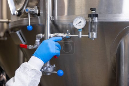 Foto de Cropped photo of a hand in a disposable nitrile glove turning the pressure relief valve lever on the brewing equipment - Imagen libre de derechos