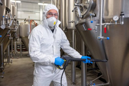 Téléchargez les photos : Experienced beer tech cleaning the external surface of the metal tank using a pressure washer - en image libre de droit