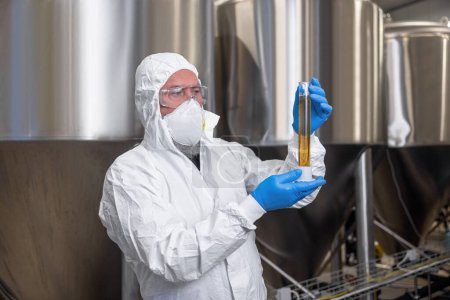 Téléchargez les photos : Waist-up portrait of a focused brewery technologist looking at a graduated cylinder in his hands - en image libre de droit