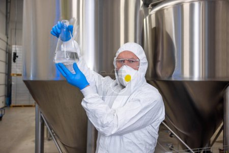 Photo for Waist-up portrait of a brewer holding a glass flask with transparent liquid in his hands - Royalty Free Image
