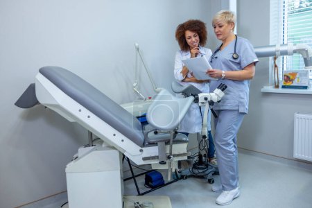 Photo for Doctors at work. Two doctors standing near gynecological chair and discussing the diagnosis - Royalty Free Image