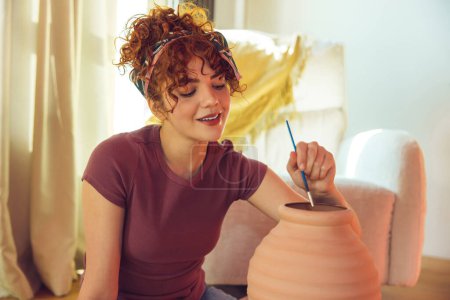Photo for Pot painting. Female artist painting the clay pot and looking involved - Royalty Free Image