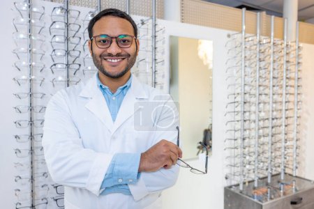 Photo for Optical store. Young african american optomestrist standing near show-case with eyeglasses - Royalty Free Image