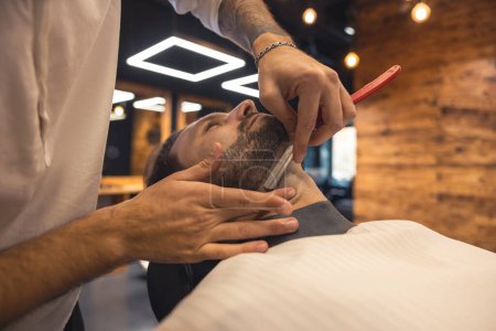 Téléchargez les photos : Trimming. Barber in the salon working on the clients beard - en image libre de droit