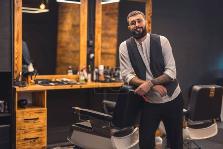 Stylish barber. Dark-haired bearded man in a stylish outfit looking confident