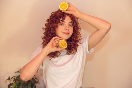 Téléchargez les photos : Love citrus. Curly-haired ginger girl with slices of orange in hands - en image libre de droit