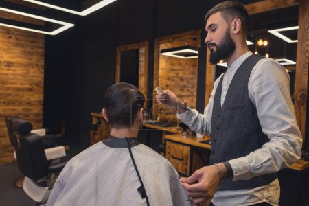 Foto de New hairstyle. Male barber combing the clients hair - Imagen libre de derechos
