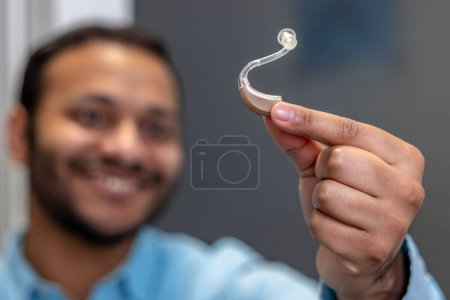 Foto de Hearing aid. Smiling young man holding a hearing aid - Imagen libre de derechos