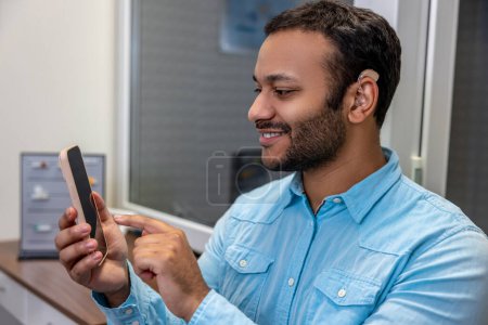 Téléchargez les photos : Contented. Smiling young man pressing buttons on the device - en image libre de droit