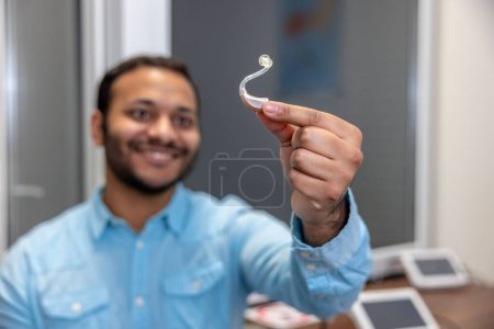 Foto de Hearing aid. Smiling young man holding a hearing aid - Imagen libre de derechos