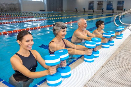 Exercise with dumbbells. Group of seniors having an exercise with dumbbels during water aerobics class