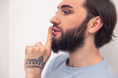 Téléchargez les photos : Portrait of a young male person with tattoo pressing the index finger to the mouth - en image libre de droit