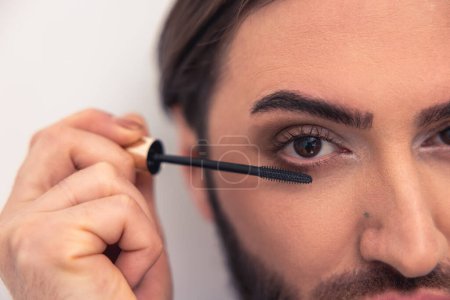 Photo for Cropped photo of a dark-haired man applying mascara to his long lashes using the wand - Royalty Free Image