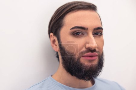 Téléchargez les photos : Portrait of a handsome calm bearded dark-haired young man wearing natural makeup during the photo shoot - en image libre de droit