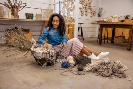 Photo for Mactame tools. Young woman sitting on the floor and looking at macrame tools - Royalty Free Image