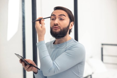 Téléchargez les photos : Serious focused cute young male person using a thin brush for the eye makeup application - en image libre de droit