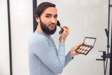 Photo for Waist-up portrait of a cute guy applying rouge to the cheek with a bristle brush - Royalty Free Image