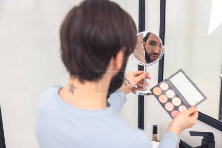 Téléchargez les photos : Back view of a transgender person holding a blusher box and mirror in his hands - en image libre de droit