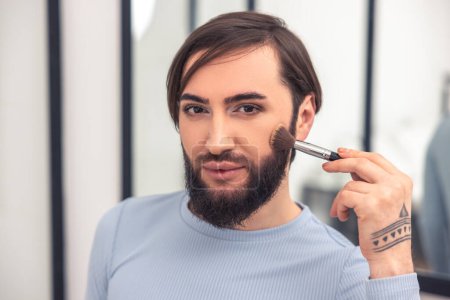 Photo for Headshot of a cute young man applying powder to the cheek with a makeup brush - Royalty Free Image