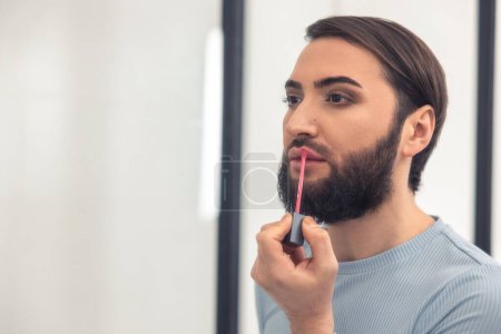 Photo for Portrait of a male person coloring lips with a pink lip gloss in the room - Royalty Free Image