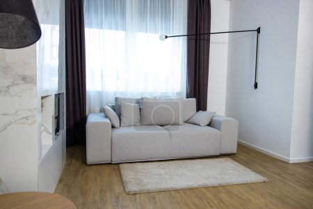 Téléchargez les photos : Canapé confortable gris avec plusieurs coussins situés par une grande fenêtre avec les rideaux blancs - en image libre de droit