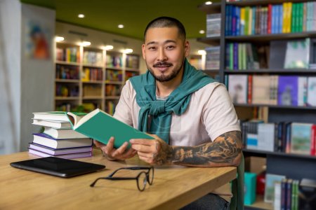 Foto de En la biblioteca. Hombre asiático leyendo libro en la biblioteca - Imagen libre de derechos