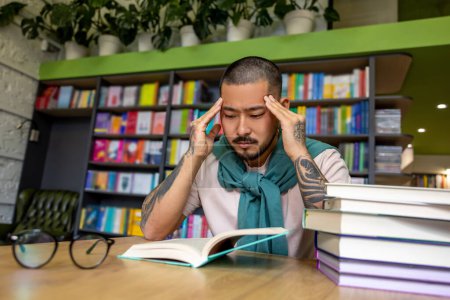 Foto de En la biblioteca. Hombre asiático leyendo libro en la biblioteca - Imagen libre de derechos