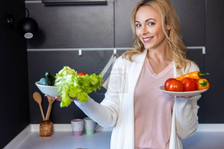 Téléchargez les photos : Portrait taille haute d'une femme joyeuse tenant deux assiettes avec des légumes frais à la main - en image libre de droit